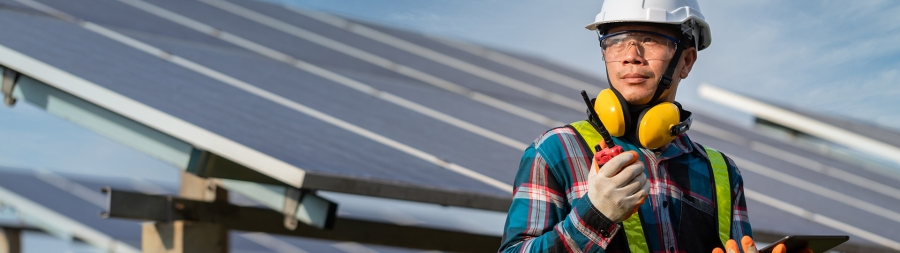 A field service engineer in safety clothing and solar panels are in background